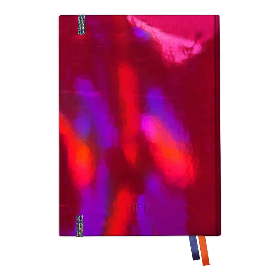 A hardcover notebook with an abstract, metallic cover featuring a blend of magenta, purple, and red colors. It has a blue and orange ribbon bookmark hanging from the bottom right corner, set against a plain white background.