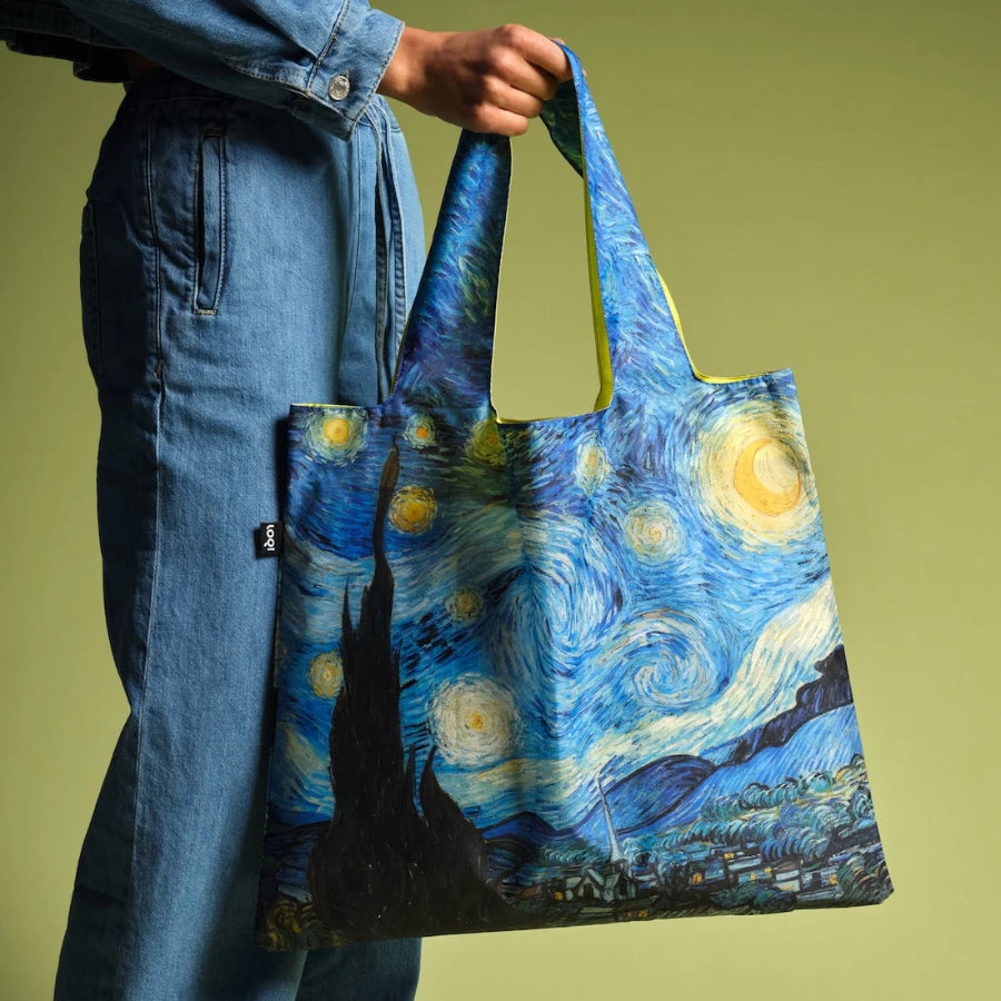 Person holding a tote bag with 'Starry Night' design against a green background