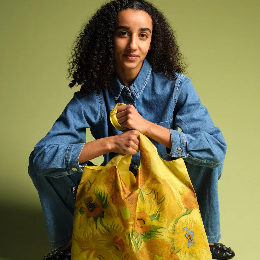 Person holding a yellow floral bag against a green background