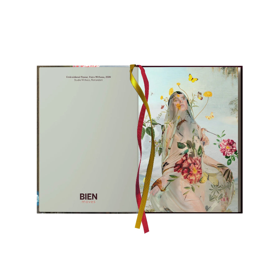 An open hardcover book or journal from BIEN, showing a light gray left page and a right page with a vintage-style illustration of a woman surrounded by flowers and butterflies. A red and gold ribbon bookmark is tied through the center.