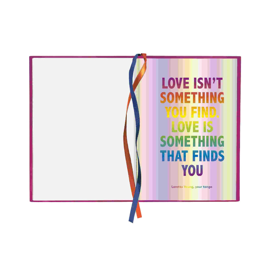 A notebook or journal with a pink cover and a rainbow-striped interior page featuring the quote 'LOVE ISN'T SOMETHING YOU FIND. LOVE IS SOMETHING THAT FINDS YOU' in multicolored text.