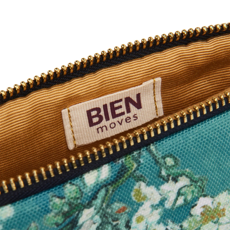 Close-up of a zipper pouch showing the interior lining, a sewn-on label reading BIEN moves, and part of a teal floral exterior pattern against a white background.