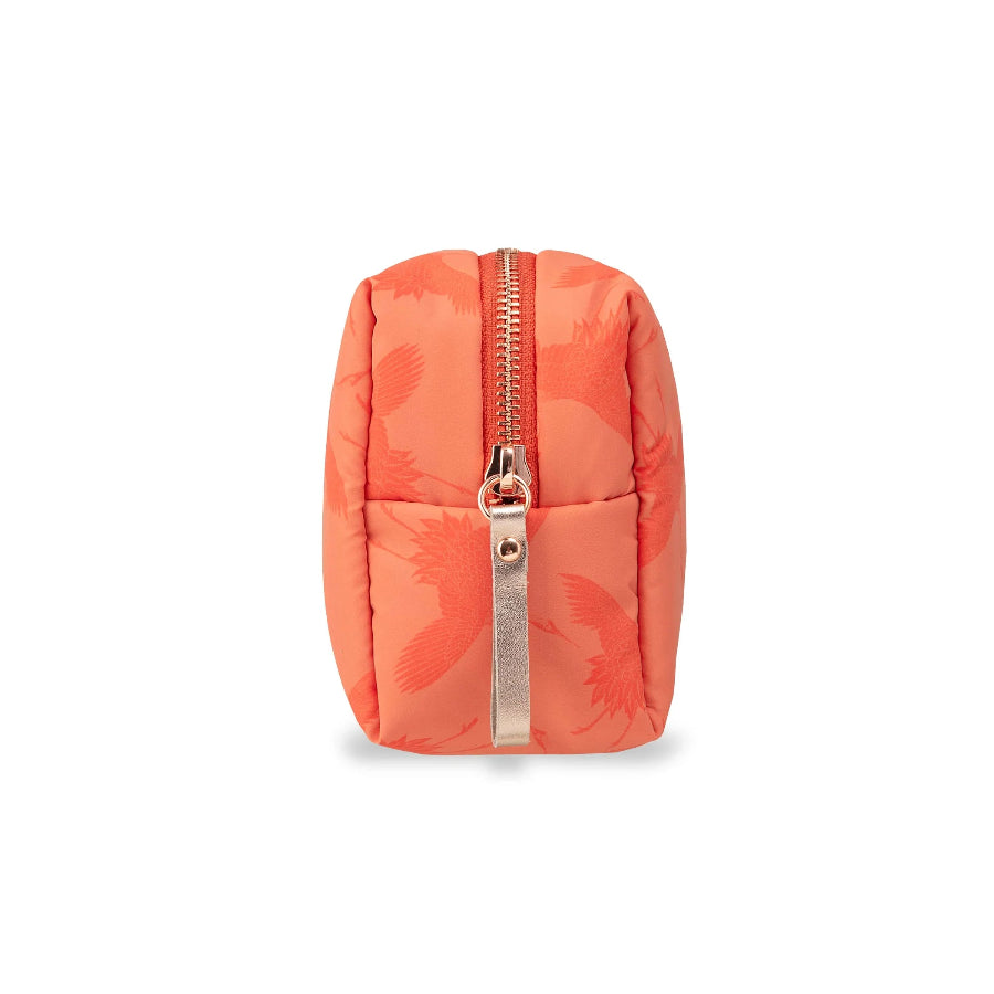 A small quilted pouch in a vibrant coral-orange color with a subtle tonal floral pattern, featuring a rose gold zipper and pull tab, shown against a plain white background.