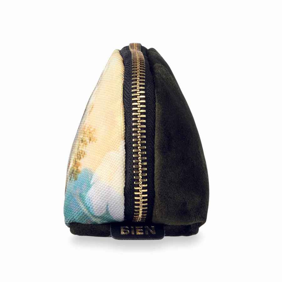 A small triangular zippered pouch with a split design: one half is black suede-like fabric and the other half features a pastel landscape print with blue, beige, and white tones. A gold zipper runs down the center, and the brand name 'BIEN' is printed in gold on the black tab at the bottom.