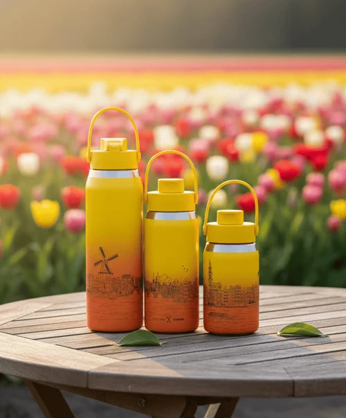 Three yellow and orange water bottles on a wooden table with a tulip field in the background