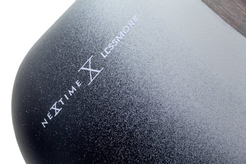 Close-up of a black textured product surface with white printed branding reading 'NEXT TIME X LESSMORE' on a white background.