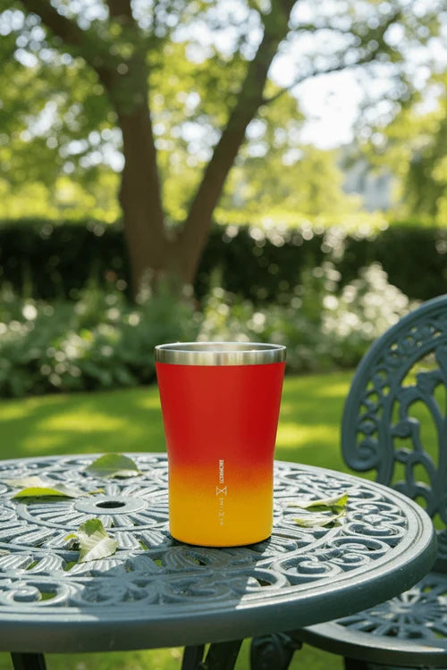 Red and yellow gradient tumbler on a garden table with greenery in the background