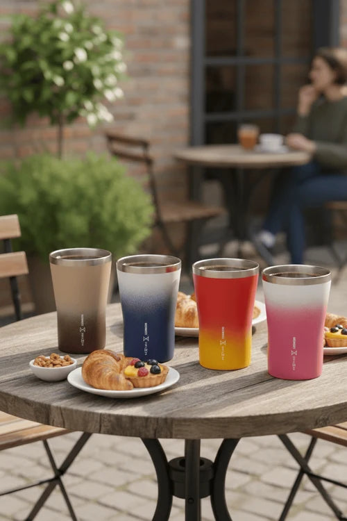 Four gradient tumblers on a table with pastries and a blurred outdoor cafe setting.