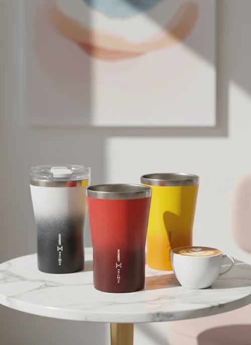 Three gradient-colored tumblers on a marble table with a blurred abstract painting in the background.