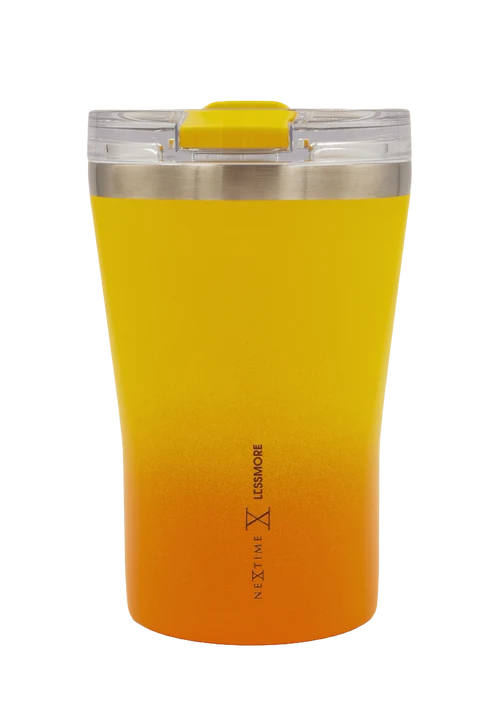 A Next Level Less More travel tumbler with a bright yellow-to-orange gradient body, a stainless steel rim, and a clear lid with a yellow flip-top spout, shown on a plain white background.