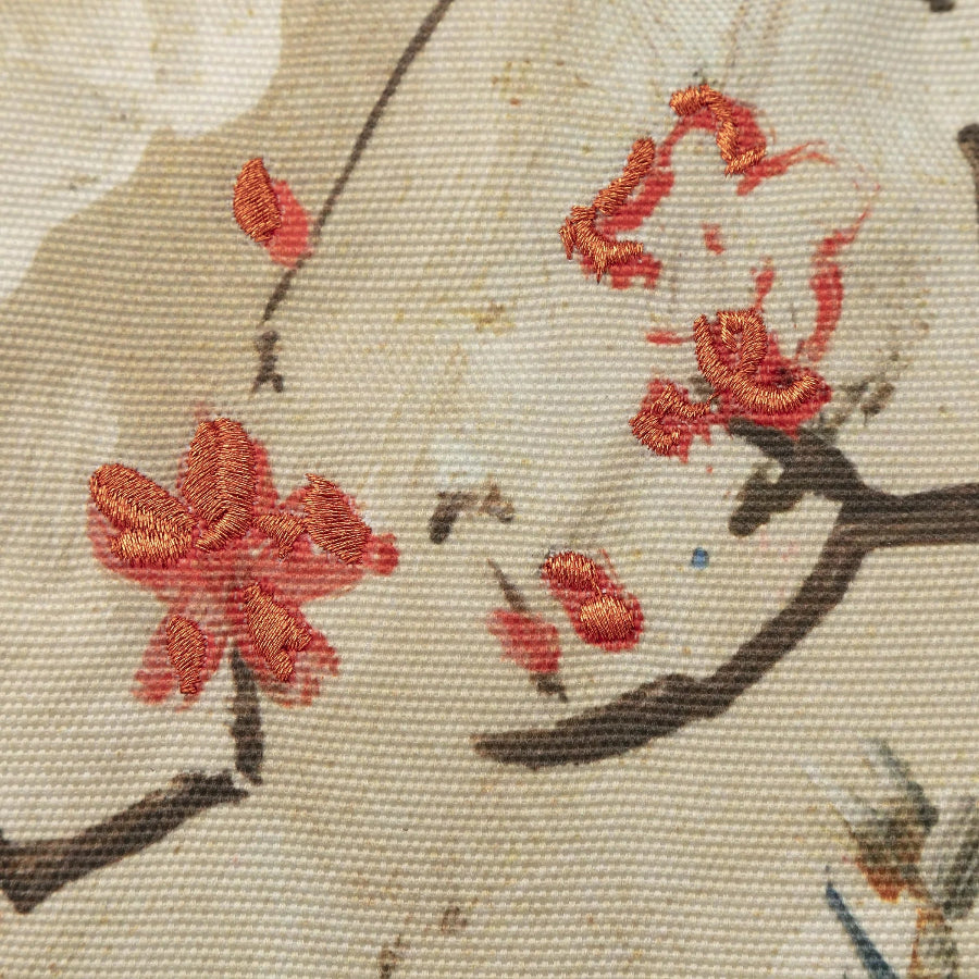 Close-up of a beige woven textile with embroidered red blossoms and dark brown branches.