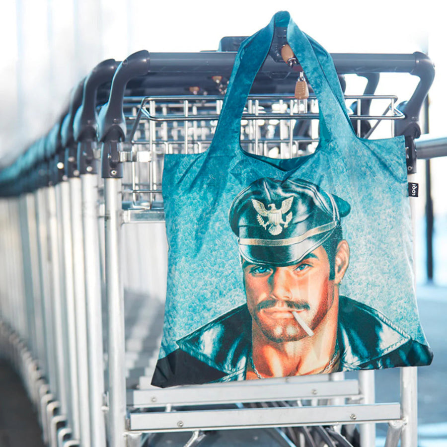 Teal tote bag with a graphic of a person in a uniform hanging on a luggage cart.