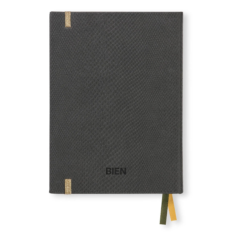 A dark gray textured notebook with a black embossed 'BIEN' logo on the front cover, featuring two small tan leather tabs and a yellow and green ribbon bookmark, shown on a plain white background.