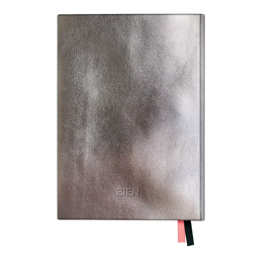 A metallic silver textured notebook with a debossed 'BIEN' logo on the front cover, featuring a pink and black ribbon bookmark peeking out from the bottom right, set against a plain white background.