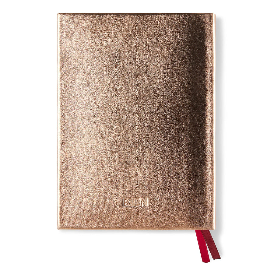 A metallic rose gold textured notebook with a red ribbon bookmark, shown on a plain white background.