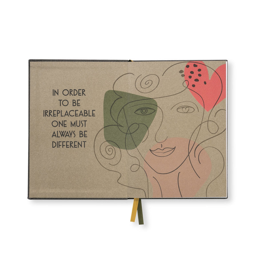 A hardcover notebook with a textured beige cover, featuring an abstract line art illustration of a face with green and pink color blocks, and the quote 'IN ORDER TO BE IRREPLACEABLE ONE MUST ALWAYS BE DIFFERENT' printed on the left. A small ribbon bookmark in green and yellow hangs from the bottom center.