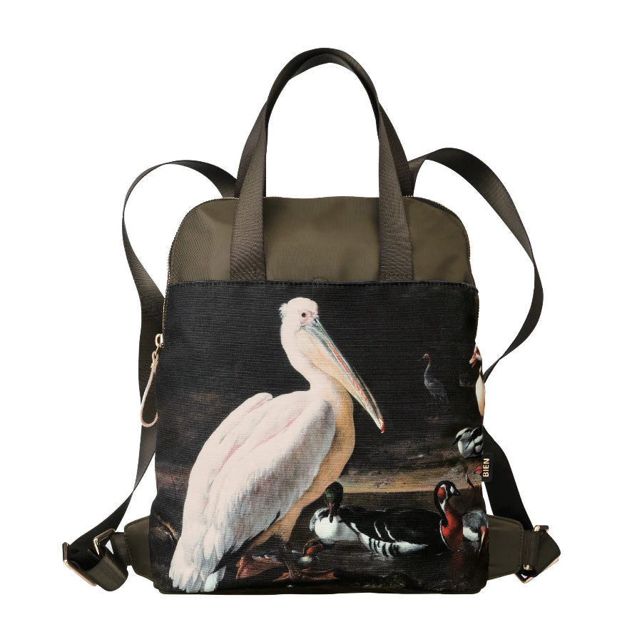 A structured canvas backpack featuring a detailed wildlife print of a white pelican and ducks on the front panel, with olive green fabric on the top and straps, set against a plain white background.