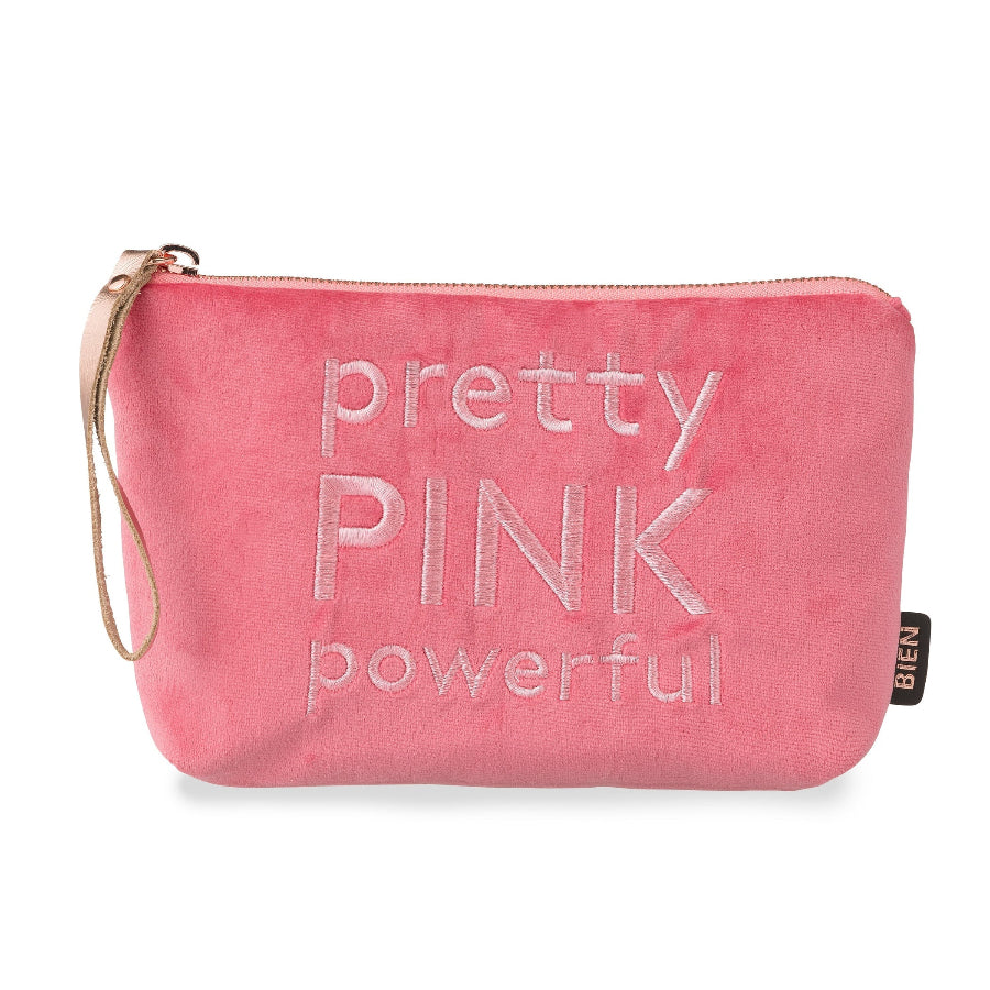 A pink velvet cosmetic pouch with the words 'pretty PINK powerful' embroidered on the front. It features a wristlet strap on the left side and a small black brand tag on the right side, set against a plain white background.