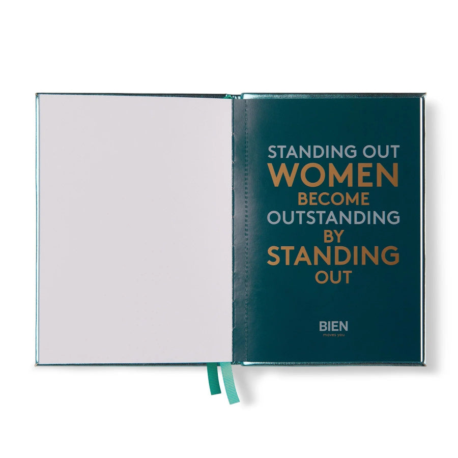 An open hardcover notebook or journal on a white background. The right page has a dark teal cover with the text 'STANDING OUT WOMEN BECOME OUTSTANDING BY STANDING OUT' in white and gold, and the brand name 'BIEN' at the bottom.