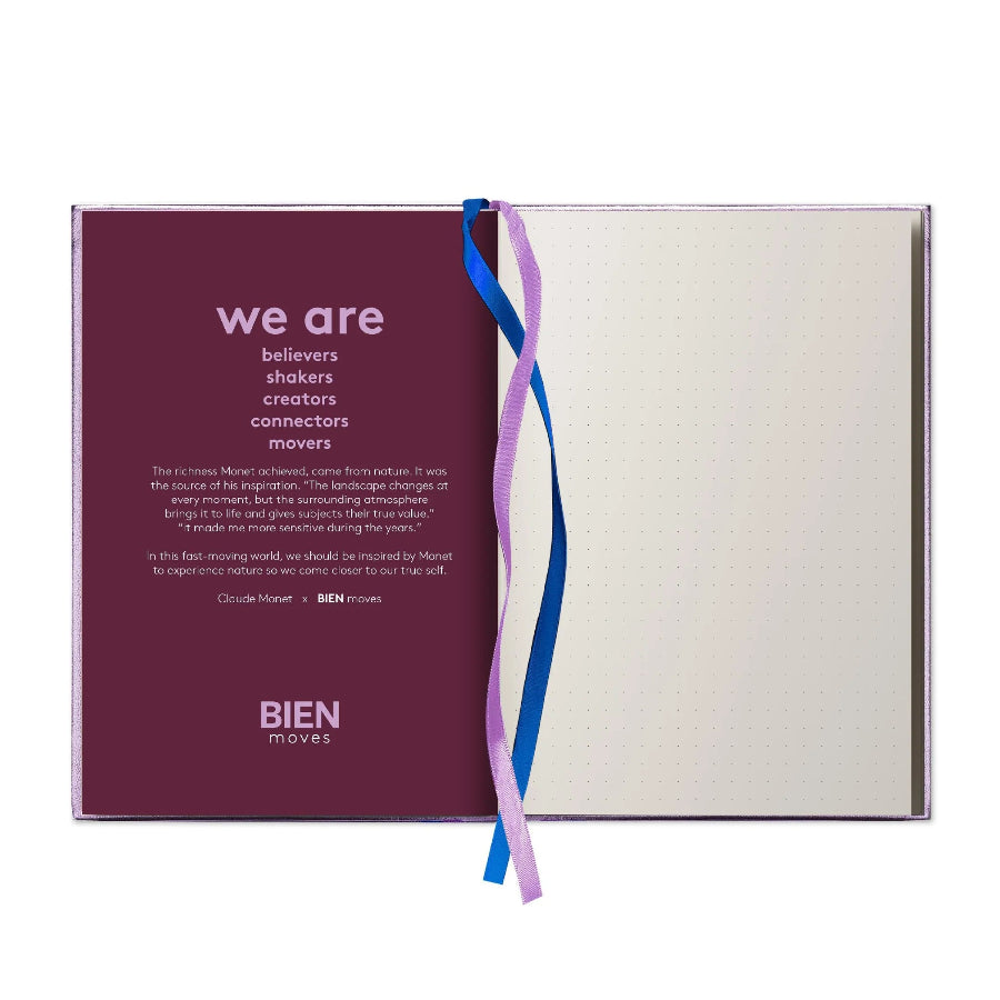 A clear acrylic notebook or journal cover shown open on a white background, with a deep burgundy left panel reading 'we are' and 'BIEN moves,' a cream dotted interior page on the right, and two ribbon bookmarks in blue and lavender tied through the center.
