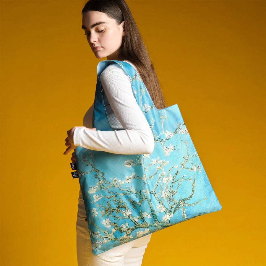 Woman holding a blue tote bag with floral design against a yellow background