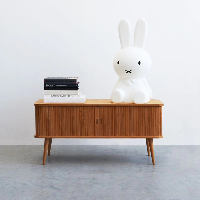 Wooden sideboard with a white rabbit sculpture and books on a plain background